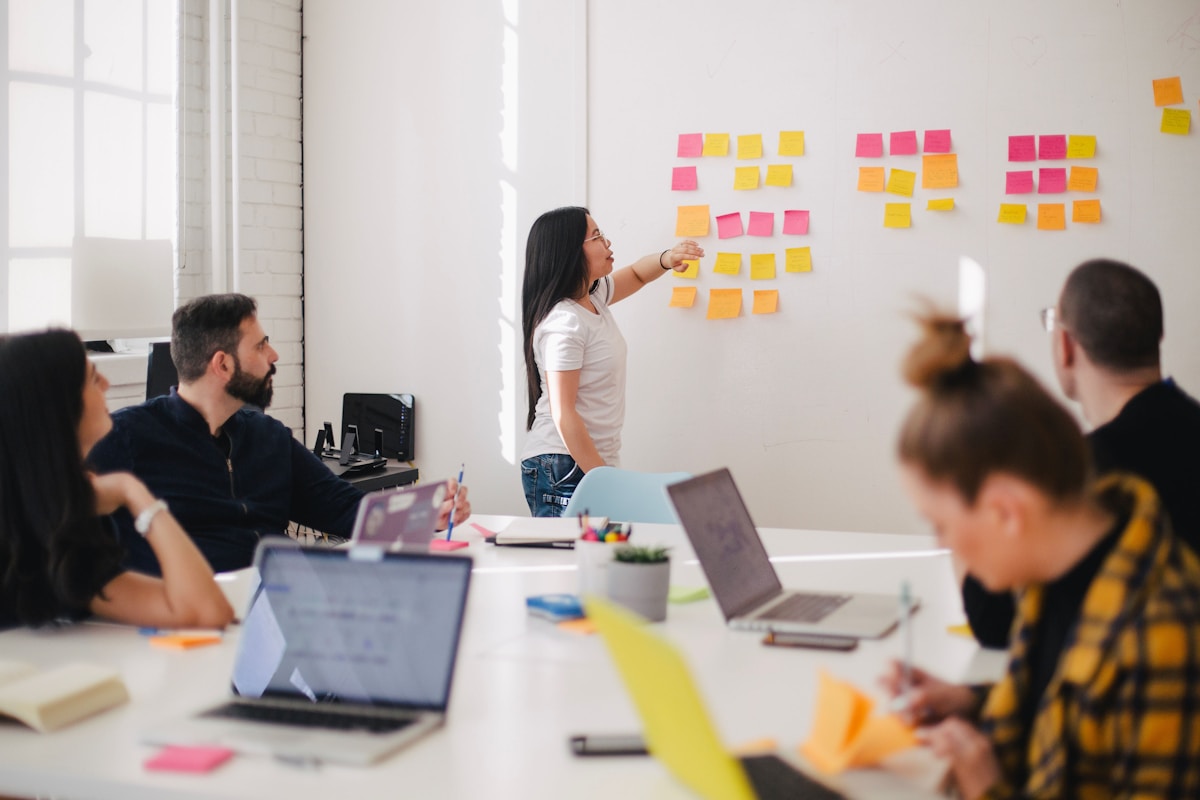 Woman presenting ideas on a whiteboard with colorful sticky notes to colleagues in an office. — Vireo Homes