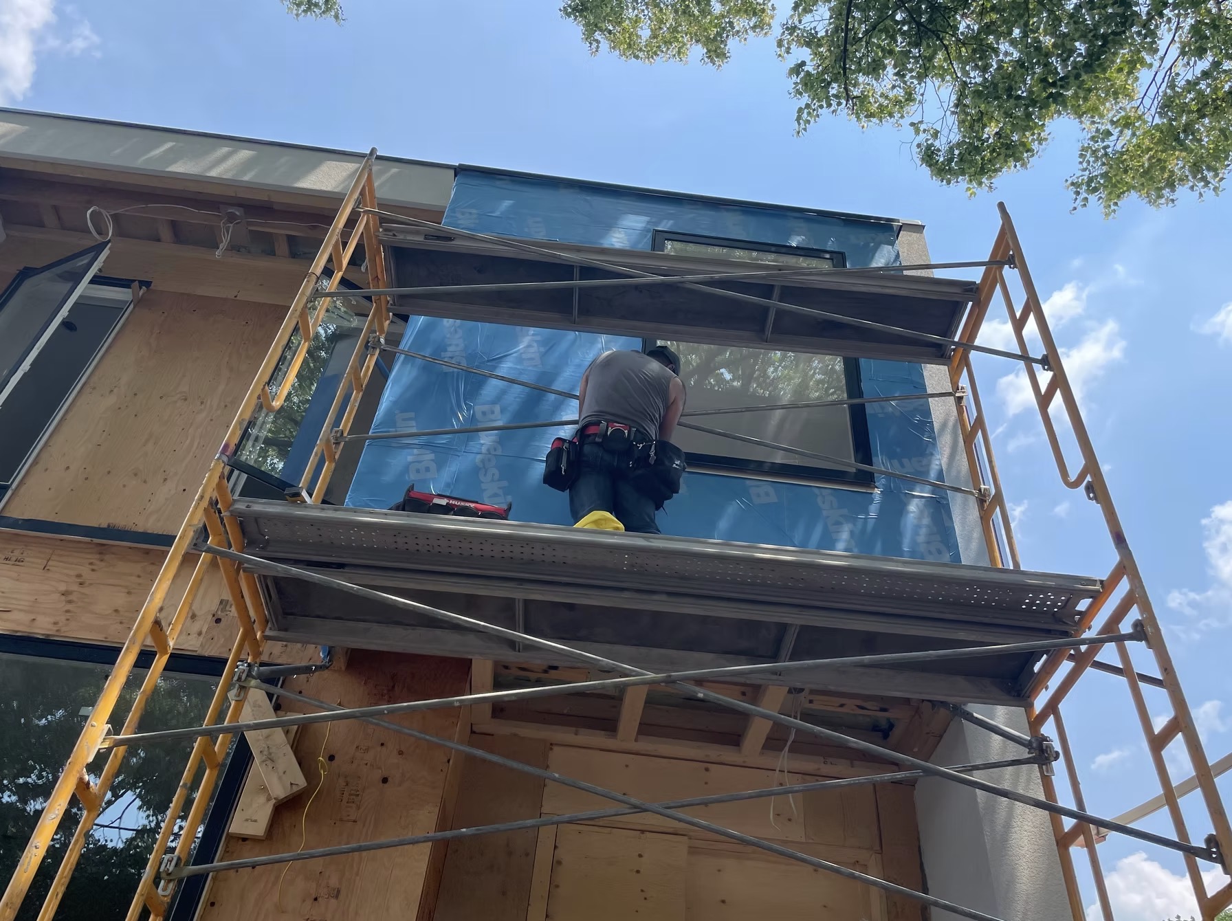 Construction worker on scaffolding installing blue house — European window and door project, Vireo Homes GTA