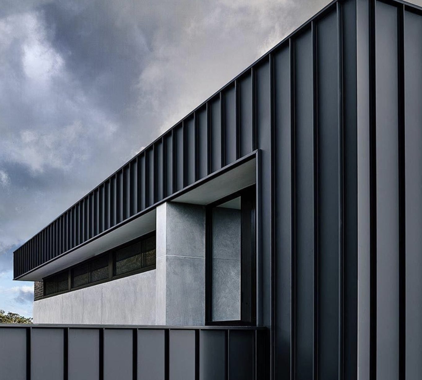 Modern building facade with dark grey vertical metal paneling and a — Vireo Homes exterior cladding systems